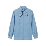 The Tiny Finch Charlie blouse in light blue cotton denim featuring a neck tie, patch pockets, and gathered cuffs.