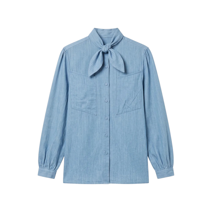 The Tiny Finch Charlie blouse in light blue cotton denim featuring a neck tie, patch pockets, and gathered cuffs.