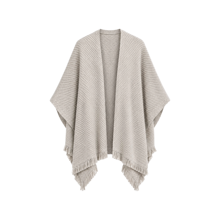 The Tiny Finch Cape Sand is a beige knitted open-front poncho featuring a textured ribbed pattern and fringe hem.