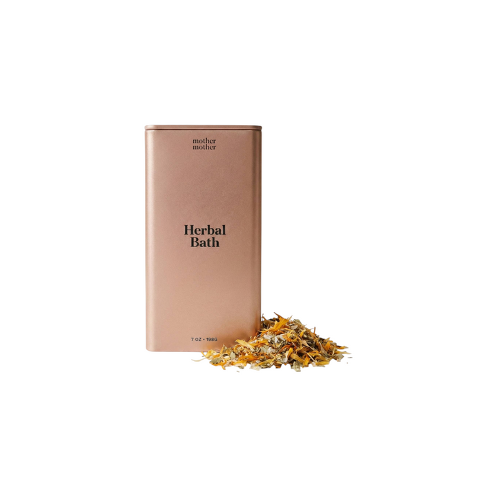 The Tiny Finch organic herbal sitz bath in a rose gold tin with a pile of dried healing herbs on a white surface.