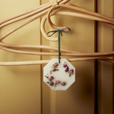 The Tiny Finch Damask Rose scented botanical wax palet hanging from a wooden hanger with dried rosebuds embedded.