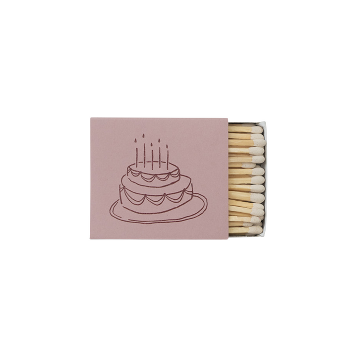 The Tiny Finch matchbox in dusty pink featuring a whimsical brown line-art illustration of a birthday cake.