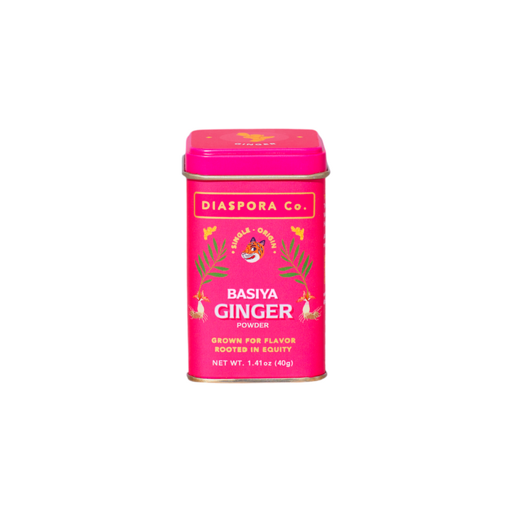 The Tiny Finch Basiya ginger powder in a bright pink tin, surrounded by a bed of finely ground golden ginger spice.