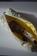 The Tiny Finch Daisy Fields hair tools bag in yellow with floral print, holding a hair straightener inside.