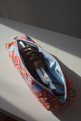 The Tiny Finch Persimmon hair tools bag in a floral quilted fabric, holding a hair straightener on a white surface.
