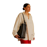 The Tiny Finch Lee black vegetable tanned leather tote bag with brass hardware worn over the shoulder by a woman.