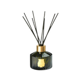 The Tiny Finch Josephine diffuser in a dark green ribbed glass bottle with a gold cap and black reed sticks.