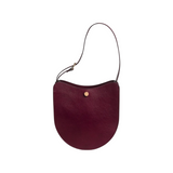 The Tiny Finch Savoie sumac red pebbled leather crossbody bag with brass hardware and adjustable shoulder strap.