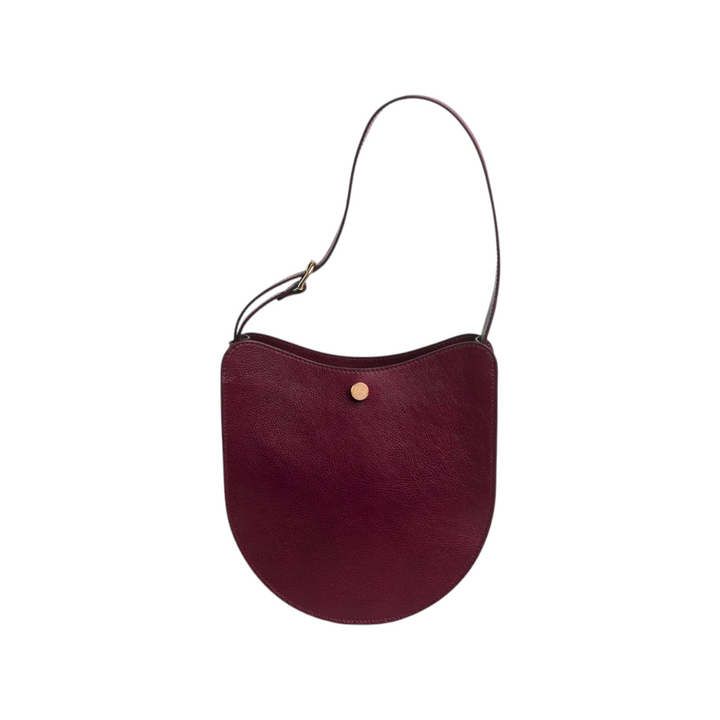 The Tiny Finch Savoie sumac red pebbled leather crossbody bag with brass hardware and adjustable shoulder strap.
