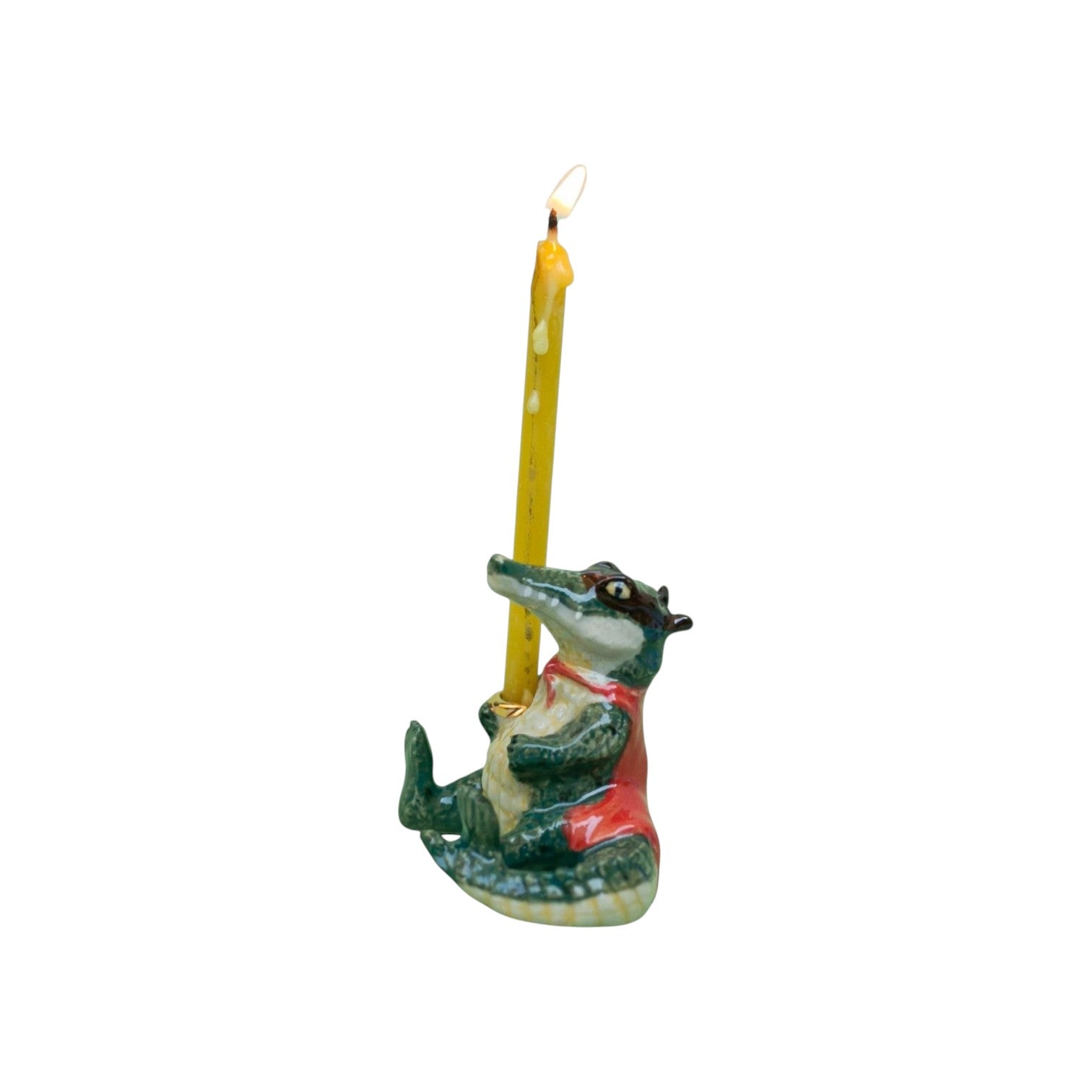The Tiny Finch porcelain alligator cake topper dressed as a bandit with a red cape holding a lit yellow candle