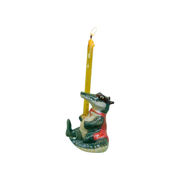 The Tiny Finch porcelain alligator cake topper dressed as a bandit with a red cape holding a lit yellow candle