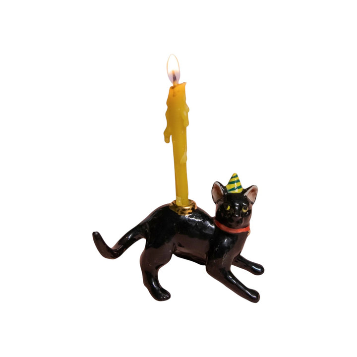 The Tiny Finch black cat cake topper wearing a party hat with a lit yellow candle on its back