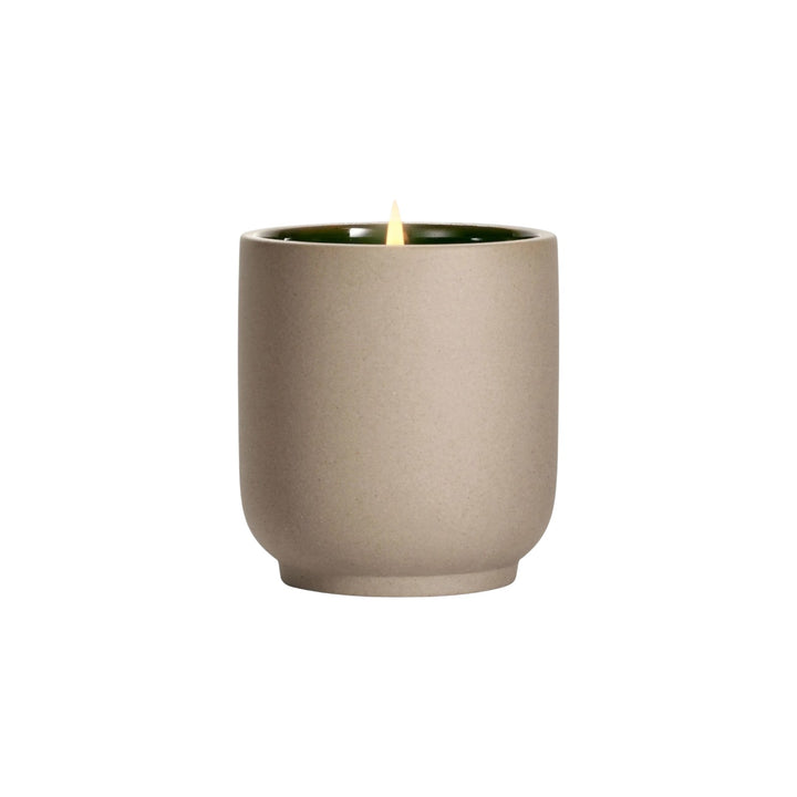 The Tiny Finch Cece candle in a beige kiln-fired ceramic vessel with a green interior and a lit organic cotton wick.