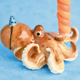 The Tiny Finch ceramic octopus cake topper in brown with a spiral peach candle holder on a blue background.