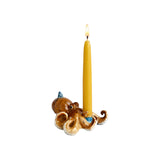 The Tiny Finch ceramic octopus cake topper in brown and cream with a lit yellow taper candle, isolated on white.