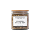 The Tiny Finch Cowgirl Bread Dip seasoning mix in a glass jar with a bamboo lid, featuring sun-dried tomato and herbs.