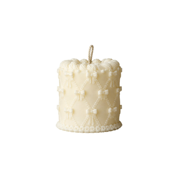 The Tiny Finch cream cake candle featuring a decorative lattice pattern with small bows and piped frosting details.