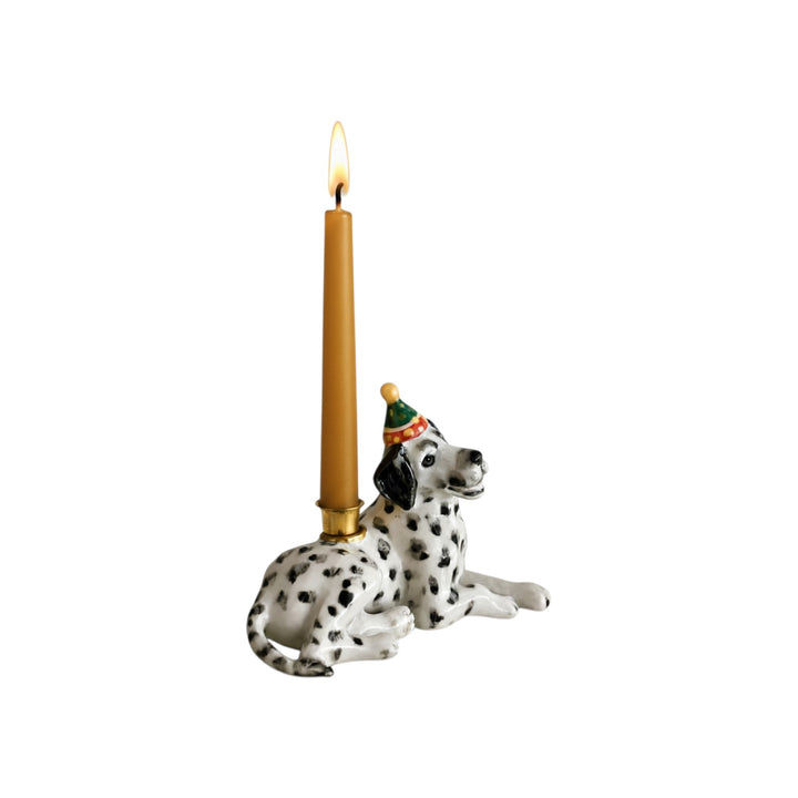 The Tiny Finch handcrafted ceramic Dalmatian cake topper with a party hat holding a lit birthday candle.