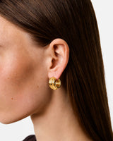 The Tiny Finch Elenora gold-plated sterling silver hoop earrings with sculptural curves worn on a model ear.