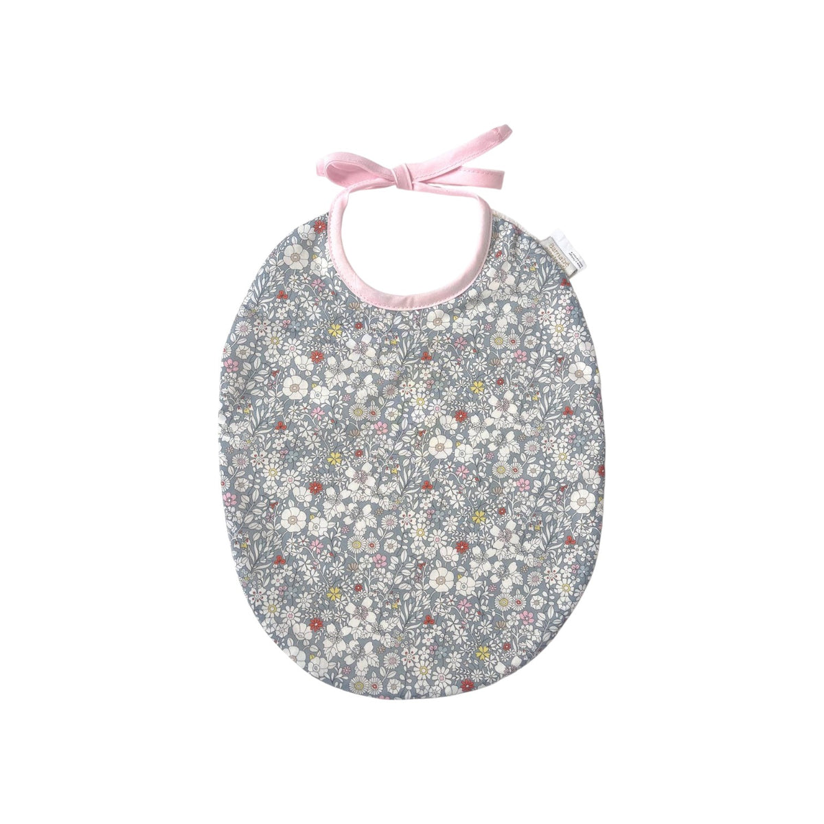 The Tiny Finch Bib Katie featuring a grey Liberty fabric with delicate floral patterns and soft pink tie closure.