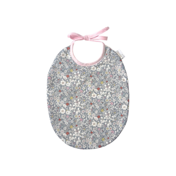 The Tiny Finch Bib Katie featuring a grey Liberty fabric with delicate floral patterns and soft pink tie closure.