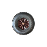 The Tiny Finch Toasty Horchata Almond Butter dark chocolate bar in a geometric flower shape on a dark ceramic plate.