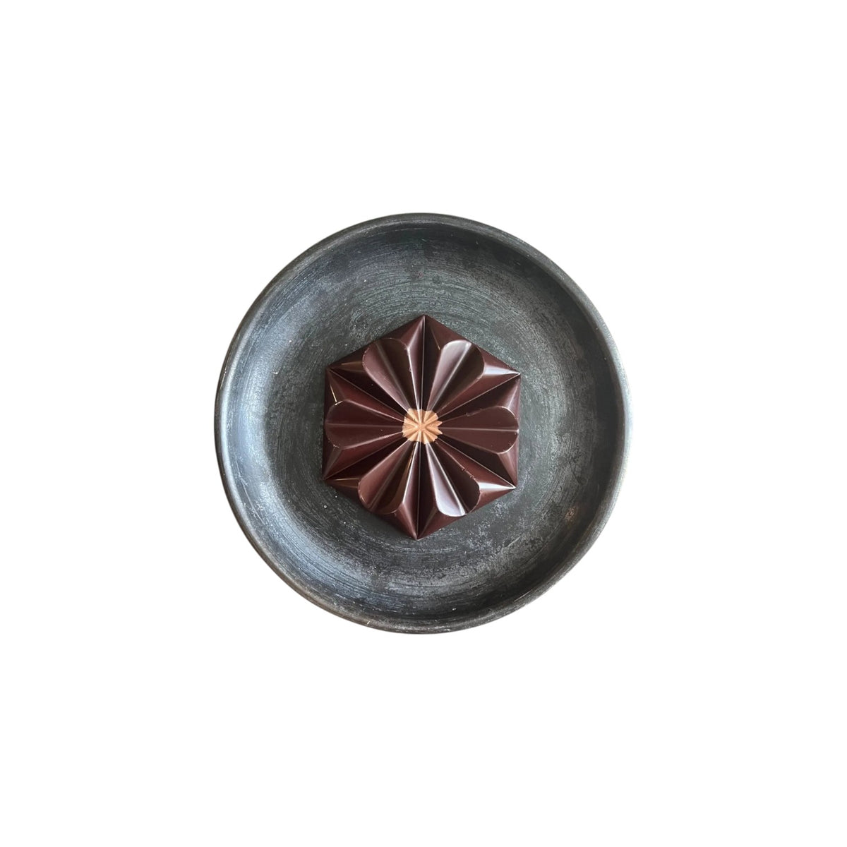 The Tiny Finch Toasty Horchata Almond Butter dark chocolate bar in a geometric flower shape on a dark ceramic plate.