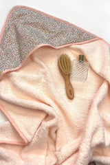 The Tiny Finch Juliette baby towel in soft peach sponge with floral Liberty fabric hood, brush, and perfume bottle.