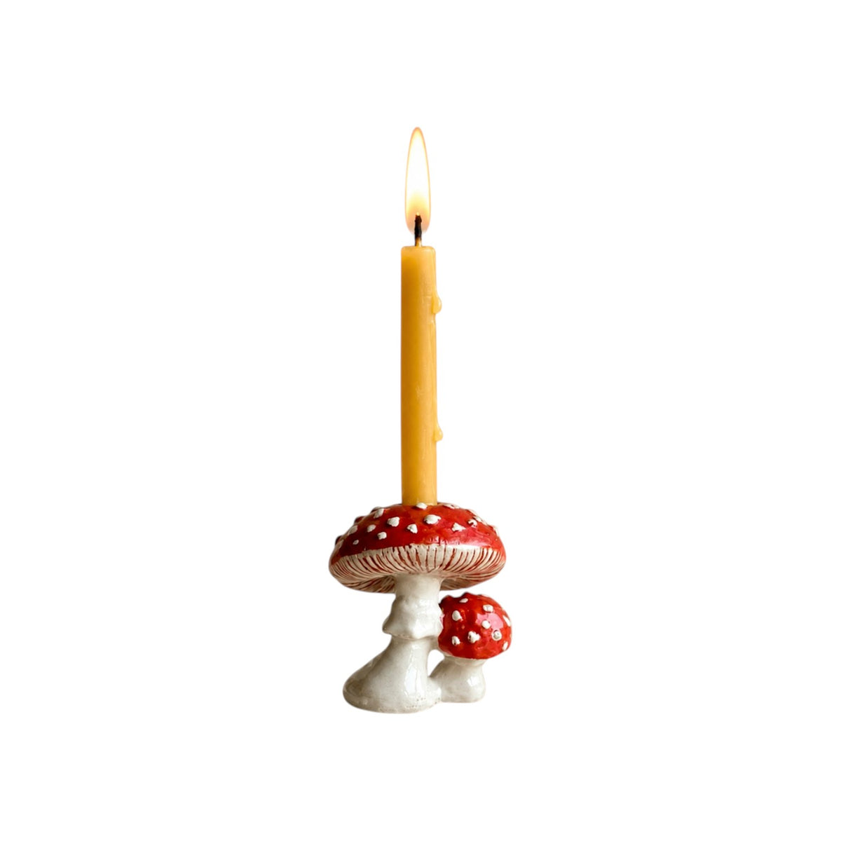 The Tiny Finch mushroom cake topper featuring a red and white toadstool design with a lit yellow taper candle.