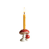 The Tiny Finch mushroom cake topper featuring a red and white toadstool design with a lit yellow taper candle.