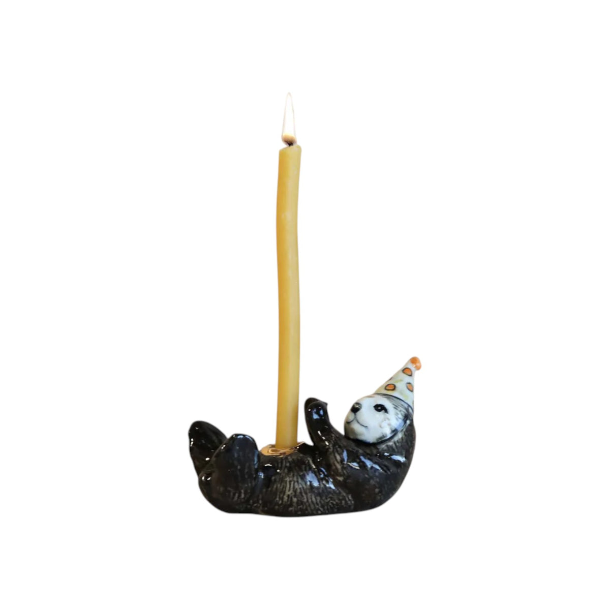 The Tiny Finch porcelain otter cake topper wearing a party hat, holding a tall yellow birthday candle.
