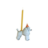 The Tiny Finch porcelain poodle cake topper wearing a striped party hat with a lit yellow birthday candle