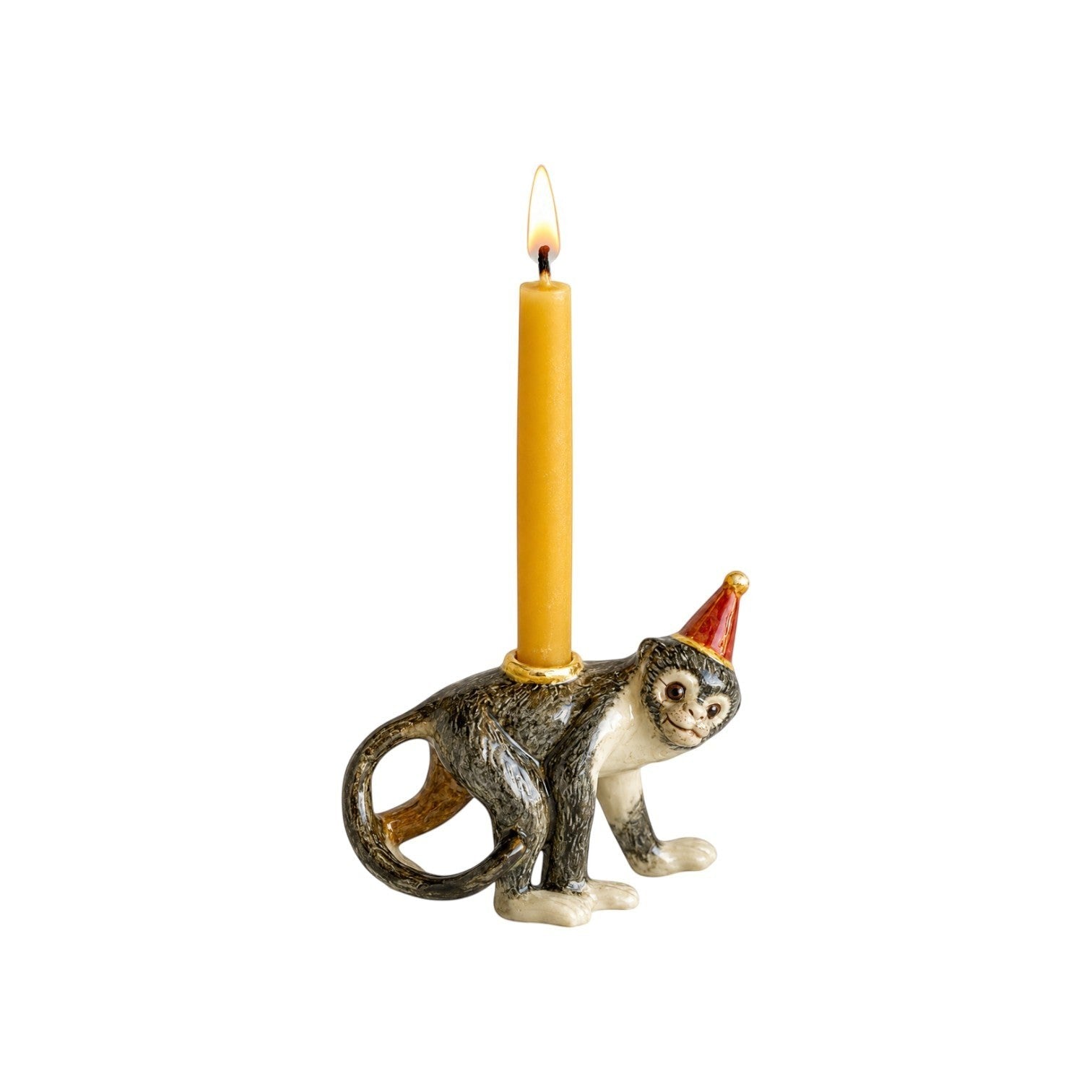 The Tiny Finch hand-painted porcelain monkey cake topper wearing a party hat with a lit yellow birthday candle