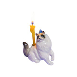 The Tiny Finch Ragdoll cat cake topper with a party hat and a lit yellow candle for birthday celebrations.