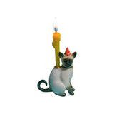 The Tiny Finch Siamese cat cake topper with a party hat and a lit yellow candle for birthday celebrations.