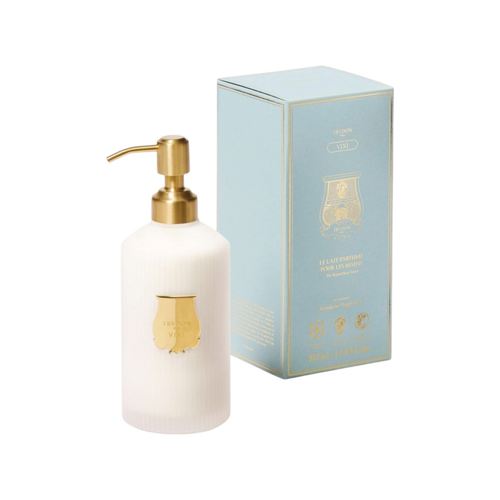 The Tiny Finch Trudon Vixi scented hand lotion in a white ribbed bottle with a gold pump next to its light blue box.