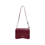 The Tiny Finch Val crossbody bag in deep sumac red leather with a solid brass hexagonal clasp and adjustable strap.